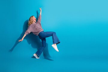 Naklejka premium Young woman in casual sweater jeans jumps with joy against blue background