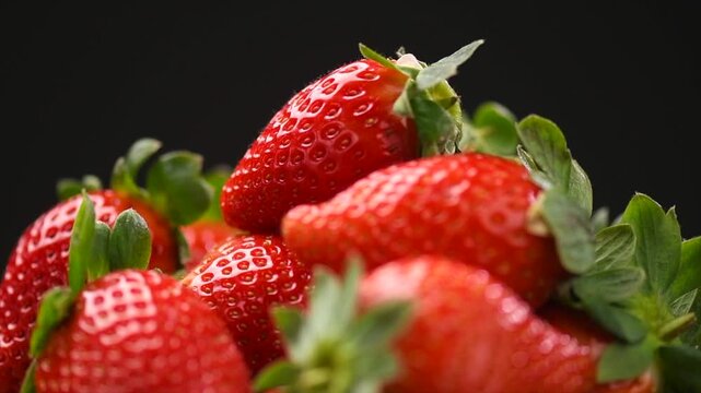 Strawberry, fresh ripe strawberries rotating over black background close-up. Organic Vegetarian healthy food backdrop, macro shot, slow motion. Delicious bio berry.  
