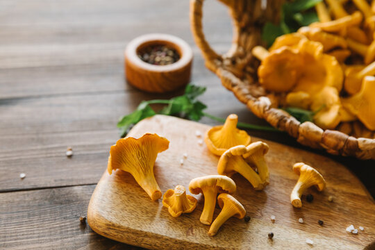 Fresh chanterelle mushrooms on a wooden board and in a basket on a dark table, rustic harvest scene, healthy cooking ingredients, organic forest food, autumn season. Top view, flat lay, copy space.