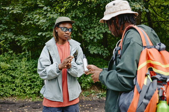Two young adult Black men hiking in forest, using insect repellent spray. Image represents outdoor recreation and is suitable for eco tourism marketing campaigns