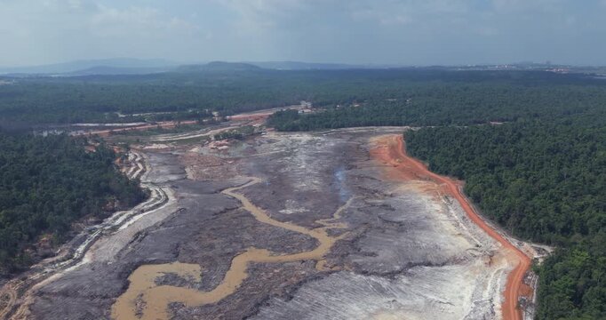 Medium aerial view of extensive deforestation and land clearing for industrial development, with visible smoke rising from the scorched earth bordering a dense tropical forest.