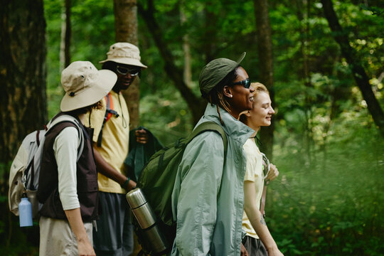 Diverse young adult friends hiking in green forest, carrying backpacks and smiling. Image represents outdoor recreation and is suitable for eco tourism marketing campaigns