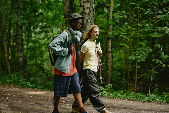 Diverse young adult couple hiking in green forest together, promoting active lifestyle and outdoor recreation. Image suitable for eco tourism and adventure gear advertising campaigns