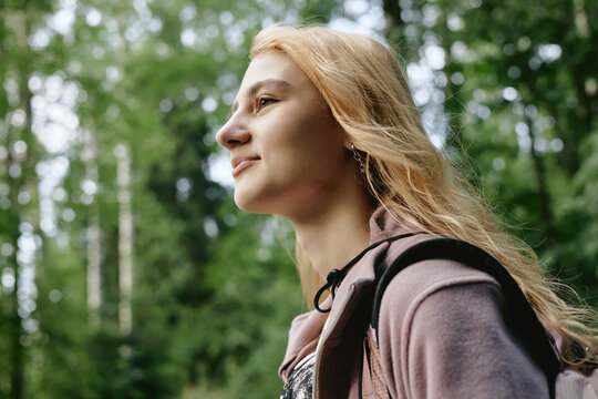 Young Caucasian woman hiking in forest, looking away with smile. Image representing outdoor recreation and mental wellbeing, suitable for ecotourism marketing, low angle shot