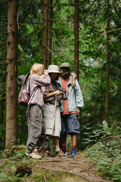 Vertical image of diverse young adult friends hiking in forest and looking at digital camera. Concept of outdoor adventure and eco tourism marketing