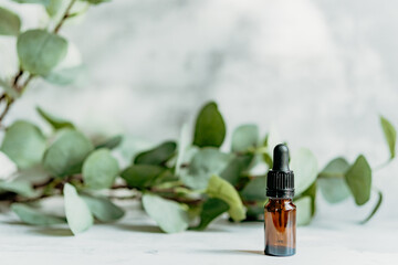 Small amber glass dropper bottle mockup on marble background with eucalyptus leaves and copy space. Natural CBD oil, eye serum, and essential oil concept. © Pure Asset