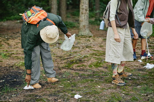 Diverse young adults picking up plastic trash in forest, promoting environmental conservation. Image suitable for eco friendly campaigns and community volunteering promotions