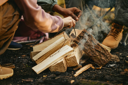 Diverse young adults building campfire in forest during hiking trip, promoting outdoor recreation. Image suitable for eco tourism campaigns and adventure gear marketing, close up shot
