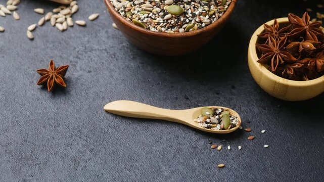 Mixed seeds and star anise in wooden bowls and spoon on dark background