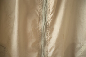 Close up of a white plastic zipper on a beige nylon windbreaker jacket.A detailed close-up shot focusing on a white plastic coil zipper running vertically down the center of a light beige or cream-col © Champ