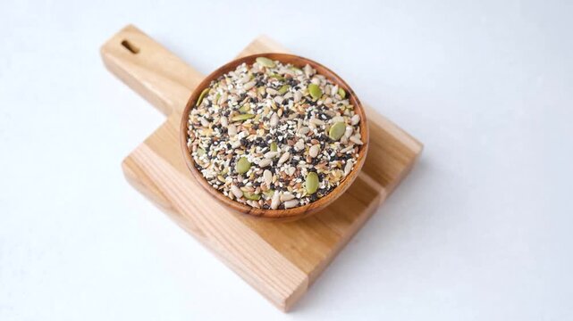 Wooden bowl filled with mixed seeds on a wooden board against a white background