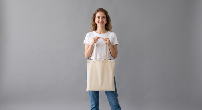 Woman holding a blank tote bag in front of gray background