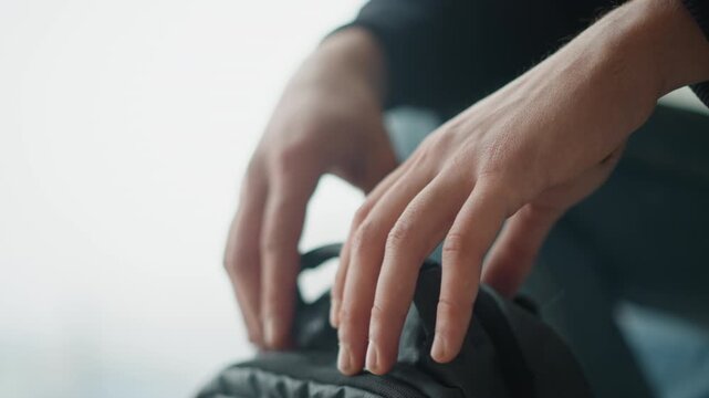 Close up of hands gripping and adjusting black fabric bag handle showing interaction with object. Hands move slightly but consistently on textured material in soft lighting emphasizing grip