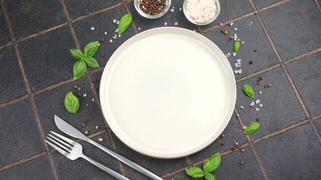 Empty plate with basil leaves, salt and pepper on dark tiled background