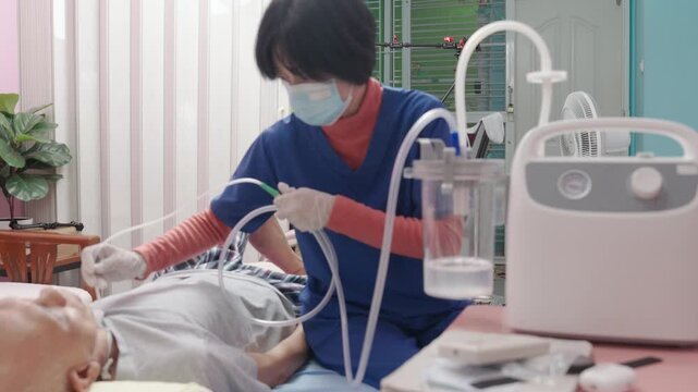 Nurse suctions mucus from a tube in the throat of a patient who had a tracheostomy and is recovering at home 