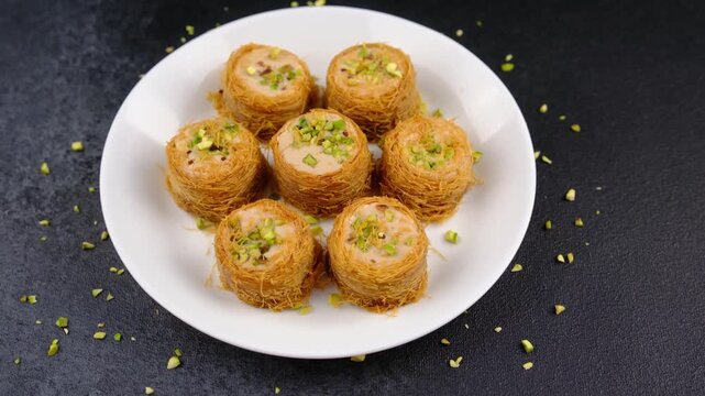 Kataifi pastries with pistachios on a white plate against a dark background
