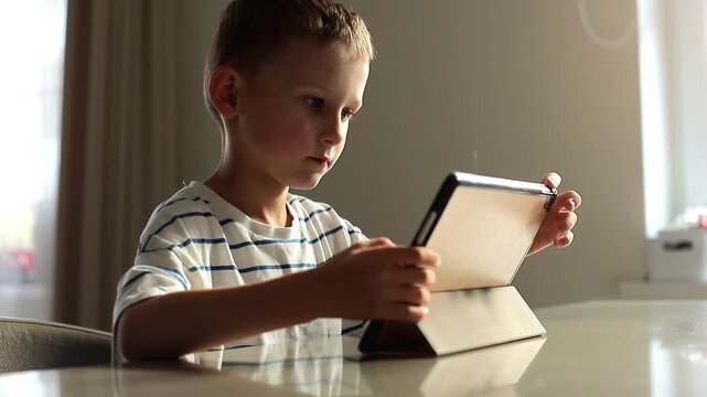 Young boy sits with a tablet at home while completing speech therapy and educational exercises, combining digital learning with language development practice.