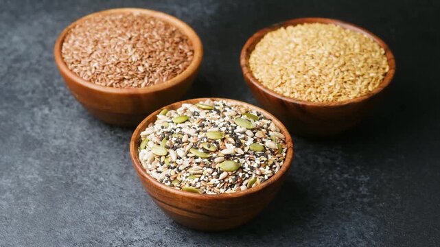 Three wooden bowls filled with different types of seeds on a dark background