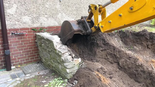 A yellow excavator bucket tears into a concrete structure during demolition work, site renovation, construction process, heavy machinery scene.