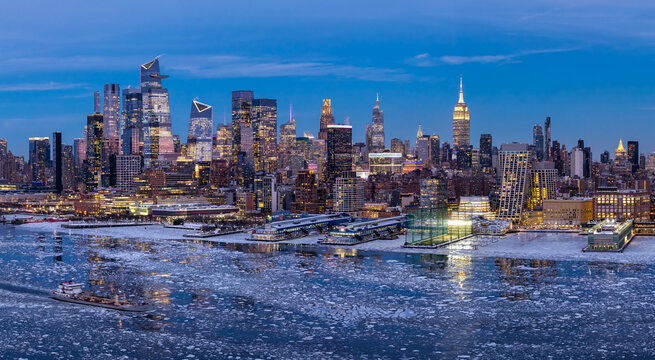 Aerial view of the Manhattan skyline at twilight in winter, with the Chelsea waterfront, ice floes covering the Hudson River and illuminated Midtown skyscrapers, New York City, USA