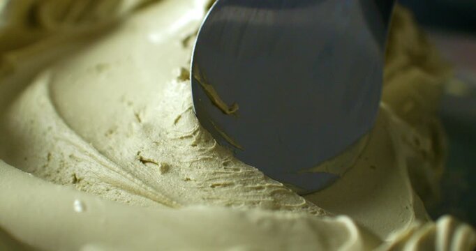 Slow Motion Close Up of Metal Spatula Mixing Thick Creamy Mixture Of Pistachios Ice cream. Macro close-up of a metal spatula moving through a smooth thick creamy mixture during food preparation.