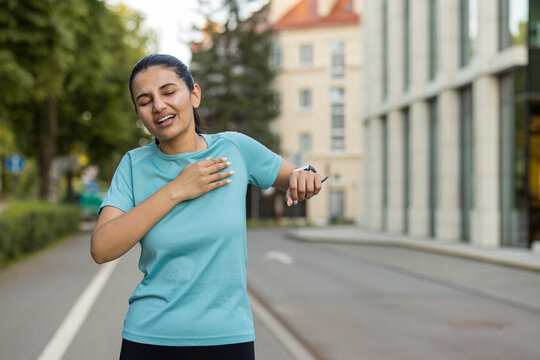 Young adult woman stopping during her outdoor run, holding her chest due to sharp pain, representing a medical emergency or health issue during exercise