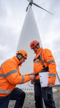 Two technicians checking climbing harness and helmet at the base of a wind turbine tower