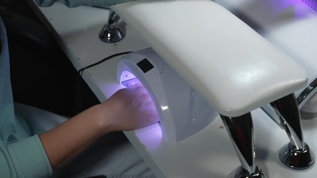 Curing gel nails under ultraviolet lamp in beauty salon as an essential step of professional manicure