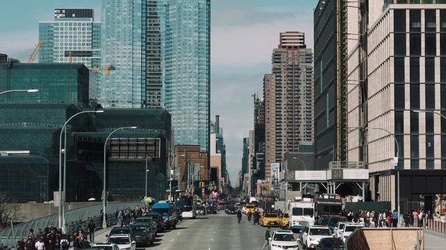 Wide street‑level motion scene of busy urban avenue showing continuous vehicular movement and dense pedestrian activity, with urban, city, street, traffic detail, showing taxi, bus, car, truck context