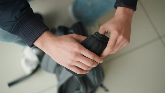 Close up of hands folding black fabric indoors. Hands manipulate material with consistent motion showing texture and drape against neutral background. Lighting is soft highlighting details