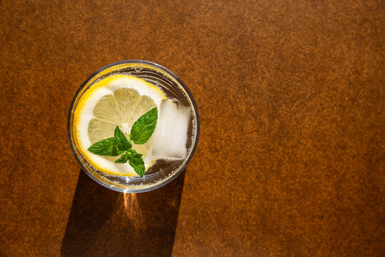 Boisson fra&icirc;che au citron, feuilles de menthe et gla&ccedil;on dans un verre, vue du dessus, fond brun, espace de copie