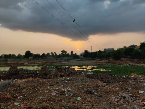   
Polluted open land with scattered garbage and debris under cloudy sunset sky showing environmental damage and waste management challenges in urban landscape