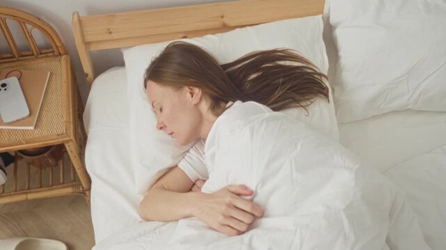 Woman sitting up in bed with arms outstretched and startled expression inside a bedroom building; surprise.