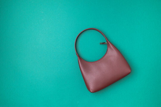 Stylish burgundy baguette bag on green background, top view with space for text. Fashionable women's leather bag, fashion accessory, wardrobe item. Autumn colors.