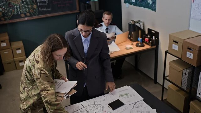 Young adult Caucasian female soldier and female specialist analyzing tactical map in military command center, high angle shot. Clip is ideal for defense industry marketing or security concepts