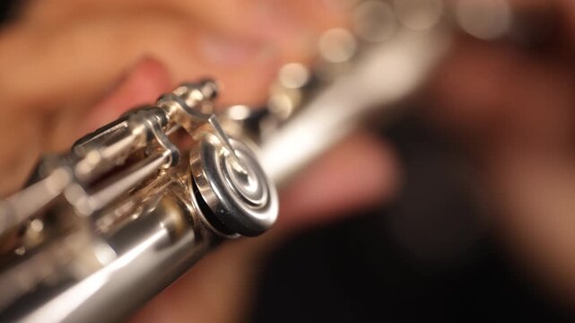 Close-up video of a flutist playing a transverse flute, focusing on hands, fingers, keys, and instrument details against a black background, capturing technique and musical movement.