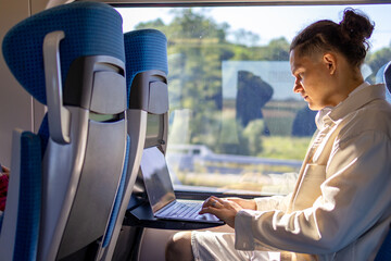 Mid adult 40s businessman working on laptop computer from train seat beside window. Concept of remote employment business travel corporate mobility and digital productivity during rail journey © Ina