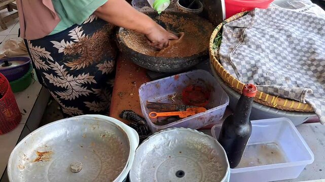 Street vendor hands grinding peanut sauce in stone mortar for traditional Indonesian food preparation.