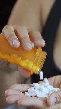 close up woman hand holding a medicine, with pours the pills out of the yellow orange medicine bottle. Stop drug use Taking Medication Caring for the health care medical concept.	