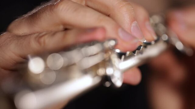 Close-up video of a flutist playing a transverse flute, focusing on hands, fingers, keys, and instrument details against a black background, capturing technique and musical movement.