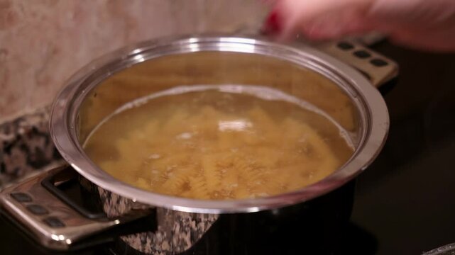 Pouring salt into boiling pasta water in pot. 