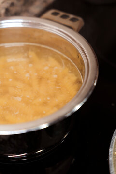 Pasta boiling in bubbling water on stove in stainless steel pot. 
