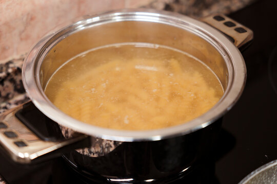 Pasta boiling in bubbling water on stove in stainless steel pot. 