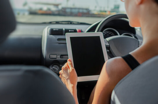 A person holds a tablet computer with a blank screen while sitting inside a car.