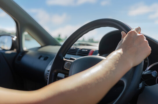 A person holds the steering wheel while driving a car on a sunny day.