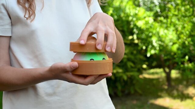 Girl holding a green dumpling shaped squishy toy in a box outdoors in a garden. Sensory fidget, tactile play and relaxing recreational activity concept. 