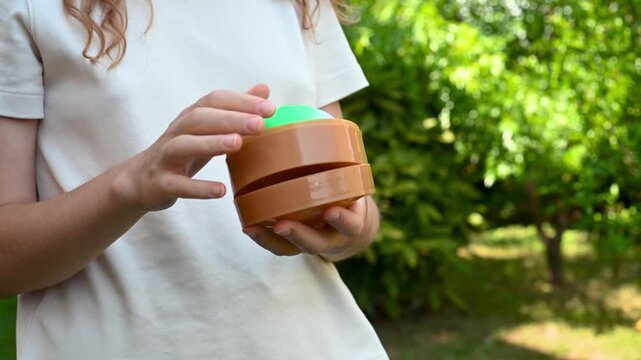 Girl holding an open box containing a colorful dumpling shaped squishy toy outdoors. Sensory toy, collecting, tactile play and playful lifestyle concept.