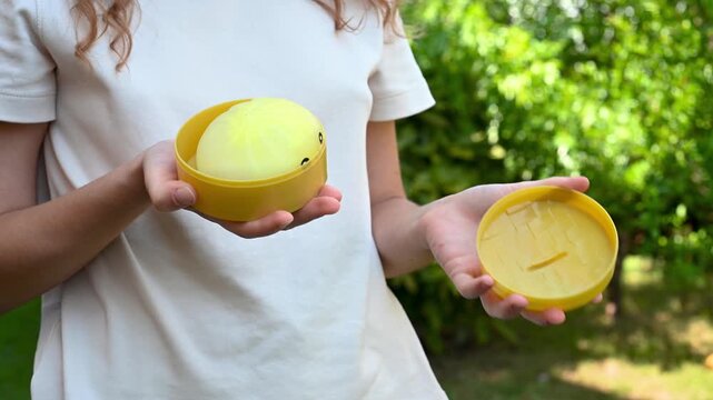 Girl opens a toy box outdoors and holds a dumpling squish toy in her hands. Close up video of a girl with a sensory fidget toy in natural sunlight.