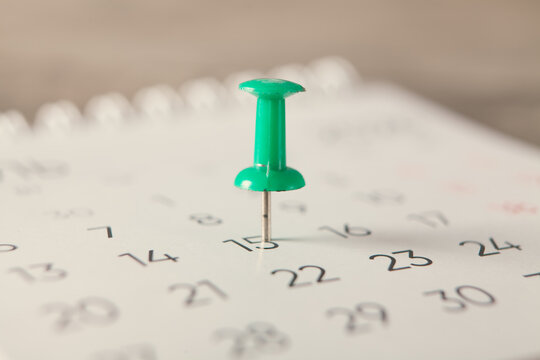 Closeup of a calendar with a green pushpin on it.