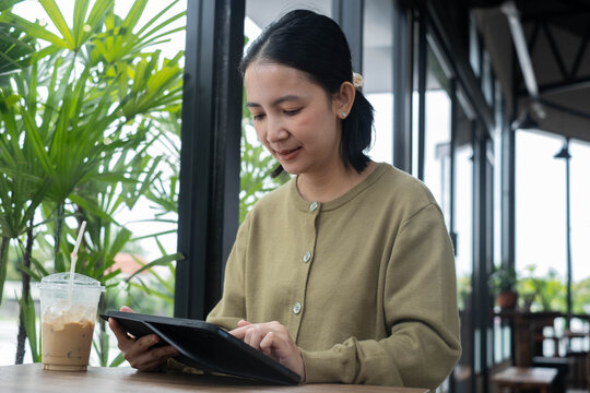 Professional woman using a tablet in a modern cafe with iced coffee, representing digital work, mobile productivity, remote business, online learning, flexible careers, and contemporary lifestyle.